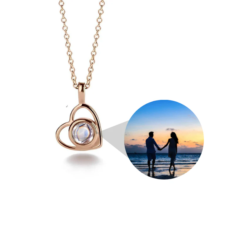 Rose gold heart-shaped necklace with a small round window showing a couple on a beach at sunset.