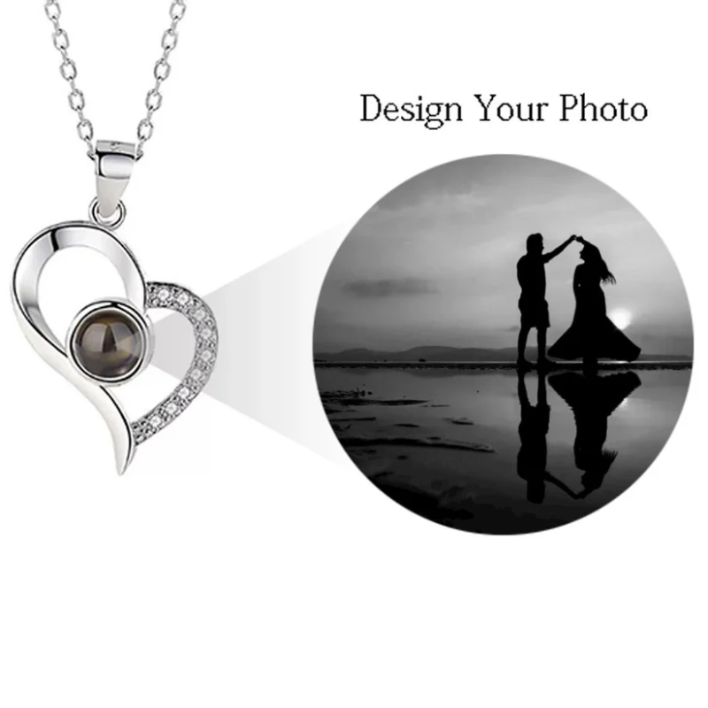 Silver heart-shaped pendant with a dark stone on a white background, next to a circular photo of a couple dancing on a beach.