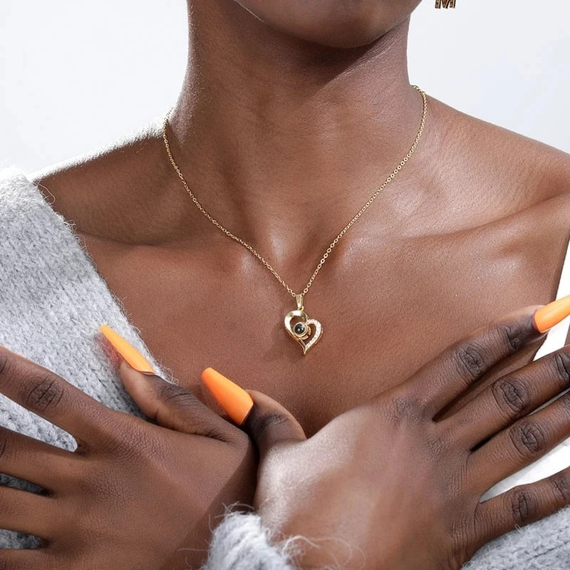 Close-up of a person wearing a gold necklace with a heart-shaped pendant, holding orange makeup brushes.